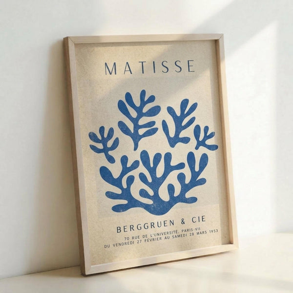 May include: Framed poster print featuring blue coral-like shapes arranged in a wreath pattern on cream background, with "MATISSE" at top and "BERGGRUEN & CIE" gallery text at bottom. Natural wood frame leaning against white wall, showing textured paper surface and exhibition details from Paris 1953.