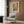 May include: Colorful Matisse-style poster in light wood frame hanging on wood-paneled wall above beige upholstered chair with geometric pillow. Artwork features vibrant collage of tropical plants, patterned chair, and decorative elements in yellows, oranges, and greens. Modern room setting with brass floor lamp and side table.