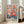 May include: Large framed art print featuring vibrant watercolor-style floral bouquet with pink, coral, orange and blue flowers against cream background, displayed on light wooden floors next to beige upholstered chair in bright room with white walls and windows. The botanical artwork shows loose, painterly brushstrokes in a modern illustrative style with "MATISSE" text at bottom in bold black letters.