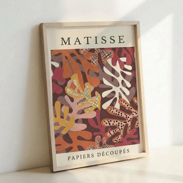 May include: Framed art print featuring abstract organic shapes in warm autumn colors - coral, burgundy, orange, yellow, and cream - with crosshatched and dotted patterns, displayed against a white wall in natural lighting. The wooden frame has a light finish and the poster shows Matisse-inspired cut-out style artwork with flowing, leaf-like forms.