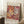 May include: Framed Matisse-style poster with abstract coral and botanical cutout shapes in warm oranges, reds, and browns, leaning against white wall corner next to small wooden stool with white coffee cup, beige textured rug below, natural lighting creating soft shadows