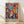 May include: Framed colorful abstract art poster leaning against white wall on light wood floor. Artwork features vibrant faces and masks in red, blue, yellow, orange, and pink with decorative foliage elements in Matisse-inspired style. Natural wood frame with clean lines. Soft natural lighting creates gentle shadows on textured white wall background.