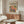 May include: Colorful modernist-style poster featuring two vibrant parrots perched on branches with tropical leaves, displayed in wooden frame above walnut credenza in minimalist living room. Cream upholstered chair and glass oval coffee table complete the mid-century modern setting with warm beige walls and natural lighting.