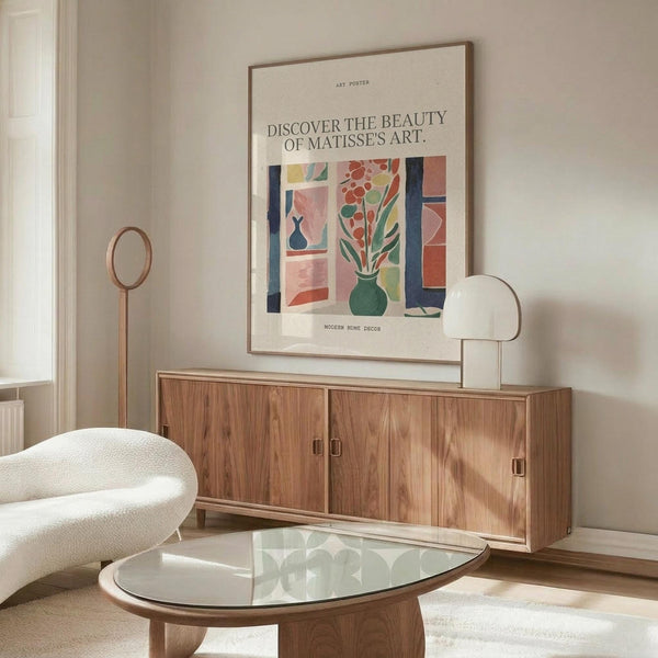 May include: Matisse-inspired art poster in thin wooden frame mounted above walnut credenza in minimalist living room. Poster features colorful window scene with green vase, pink and red flowers, blue accents on cream background. Modern white curved chair, glass oval coffee table, and white table lamp complete the Scandinavian-style interior with white walls and natural lighting.