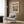 May include: Cream poster with Matisse modernist text and two colorful parrots perched on green branches against yellow background, displayed in light wood frame on textured wood wall panel above beige upholstered armchair with geometric patterned pillow, brass floor lamp and side table with open book nearby in modern living room setting