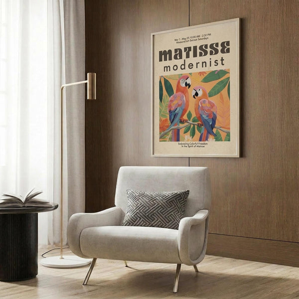 May include: Cream poster with Matisse modernist text and two colorful parrots perched on green branches against yellow background, displayed in light wood frame on textured wood wall panel above beige upholstered armchair with geometric patterned pillow, brass floor lamp and side table with open book nearby in modern living room setting