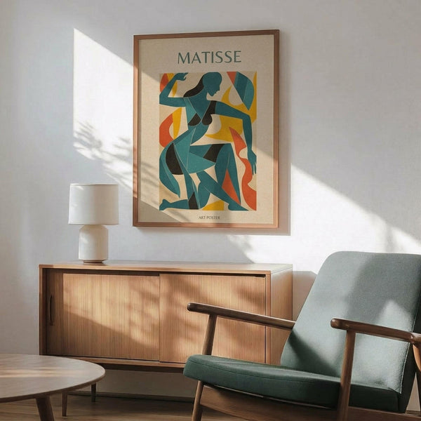 May include: Framed art poster featuring abstract cut-out style figures in teal, orange, and yellow geometric shapes on cream background, displayed above wooden sideboard with white ceramic lamp, next to mint green mid-century armchair with wooden arms, creating modern living room scene with natural sunlight casting shadows on white wall.