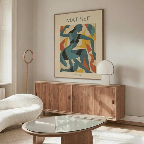 May include: Matisse art poster featuring abstract blue figure in cut-out style with colorful geometric shapes in yellow, orange, and red, displayed in thin brown frame above mid-century walnut credenza. Modern living room setting with cream textured chair, glass oval coffee table, and white table lamp. Minimalist Scandinavian interior design with neutral walls and natural lighting.