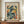 May include: Framed art poster in warm wood frame displayed on wooden console table beside white ceramic vase and stacked books. Print features abstract cut-out style figures in teal, yellow, orange and black shapes on cream background with "MATISSE" and "ART POSTER" text. Interior setting with white paneled walls and crown molding.