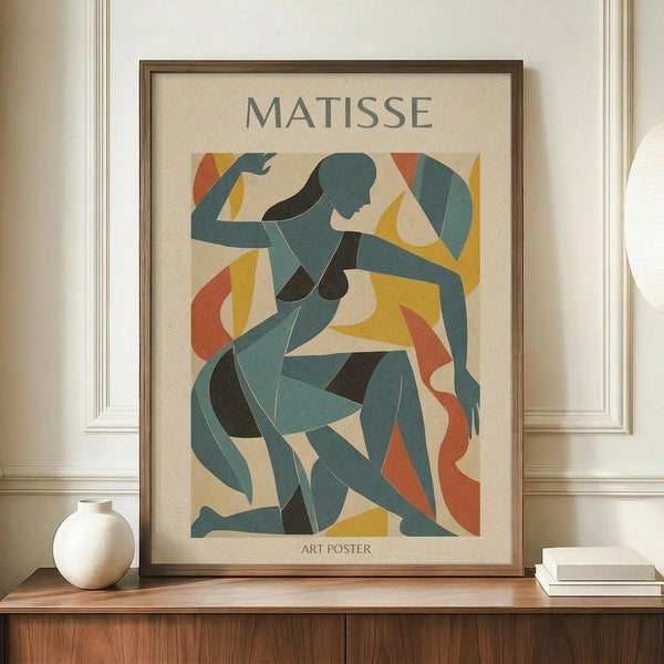 May include: Framed art poster in warm wood frame displayed on wooden console table beside white ceramic vase and stacked books. Print features abstract cut-out style figures in teal, yellow, orange and black shapes on cream background with "MATISSE" and "ART POSTER" text. Interior setting with white paneled walls and crown molding.