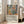 May include: Colorful art exhibition poster with abstract still life showing vases, plants, flowers and fruit in vibrant blues, greens, oranges and yellows. White wooden frame leans against beige wall next to gray sectional sofa in bright living room with large windows and wall sconce lighting.