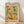 May include: Framed art poster in natural wood frame leaning against white wall on light wooden floor. Artwork features colorful still life with citrus fruits, leafy branches, bottles and bowls in Matisse-inspired style using yellows, greens, oranges and pinks on cream background. Text reads "MATISSE" at top and "ART POSTER" at bottom. Soft natural lighting creates gentle shadows on wall.