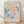 May include: Framed poster print in natural wood frame leaning against white textured wall on light wooden floor. Features abstract cut-out style artwork with flowing organic shapes in coral pink and various shades of blue on cream background. French exhibition text at top and bottom. Soft natural lighting creates gentle shadows on wall.