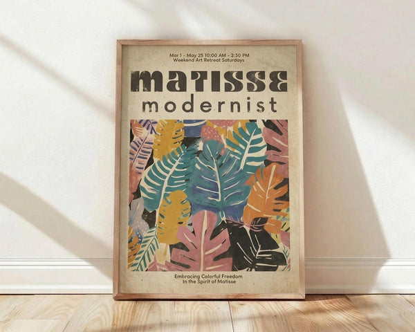 May include: Framed poster with colorful tropical leaves in Matisse-inspired cut-out style, featuring vibrant pink, teal, yellow, and orange foliage against cream background. Wooden frame leans against white wall on light wood floor with soft shadows.