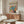 May include: Colorful botanical poster with tropical leaves in pink, orange, teal and yellow tones hanging above mid-century modern walnut credenza. Modern living room setting features white curved chair, glass oval coffee table, and minimalist floor lamp. Poster displays in thin wooden frame against white wall with natural sunlight creating soft shadows.