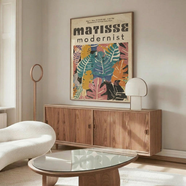 May include: Colorful botanical poster with tropical leaves in pink, orange, teal and yellow tones hanging above mid-century modern walnut credenza. Modern living room setting features white curved chair, glass oval coffee table, and minimalist floor lamp. Poster displays in thin wooden frame against white wall with natural sunlight creating soft shadows.