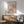 May include: Framed Matisse cut-out style art print with organic leaf and coral forms in coral, green, and navy blue colors, displayed above a mid-century modern wooden credenza with ceramic table lamp, next to a sage green upholstered armchair with wooden arms in a sunlit room with white walls