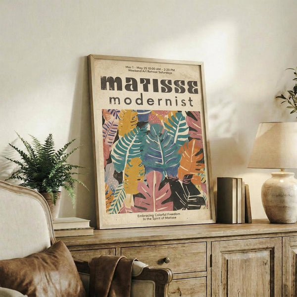 May include: Framed poster with colorful tropical leaves in pink, teal, orange, and yellow tones displayed on rustic wooden sideboard beside fern plant, ceramic vases, and stacked books in neutral-toned living room setting