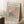 May include: Framed vintage-style exhibition poster featuring Henri Matisse's colorful paper cut-out leaf designs in coral pink, sage green, and navy blue on cream background. Wooden frame leans against white paneled wall next to coffee cup on books and cozy knit blanket on textured rug.