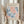 May include: Person holding framed vintage art exhibition poster featuring Matisse's papiers découpés cut-out style in coral pink and blue organic shapes against cream background. Light wood frame, dried pampas grass in other hand, neutral curtained interior setting with soft natural lighting.