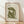 May include: Framed art print featuring olive green abstract cut-out style figure in seated pose on cream textured background, displayed in light wood frame against white wall on natural wood floor with soft window light shadows