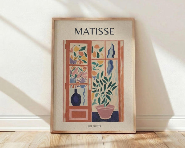 May include: Framed art poster featuring Matisse-style interior scene with colorful botanical elements viewed through window panes, displayed on light wooden floor against white wall with natural shadows. The artwork shows a potted plant, decorative vase, and stylized foliage in warm coral, blue, green and yellow tones within a natural wood frame.