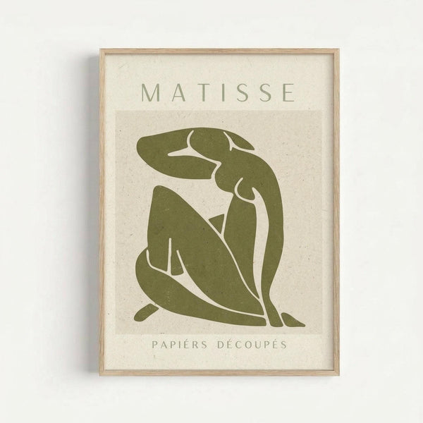 Abstract green figure in Matisse's cut-out style sits in contemplative pose against cream textured background. The simplified human form is rendered in olive green with flowing, organic shapes. Text reads "MATISSE" at top and "PAPIERS DÉCOUPÉS" at bottom in muted green letters. Displayed in thin natural wood frame against white wall.