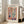 May include: Framed Matisse-inspired art poster leaning against white wall next to beige sofa. Poster features colorful cut-out style illustration of window with geometric panels showing plants, vases, and organic shapes in coral, blue, green, and pink tones. Light wood frame on hardwood floor in bright, minimalist living room with natural sunlight.