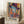 May include: Colorful artistic poster in light wood frame leaning against white wall on white fuzzy rug. Features woman with blue-tinted skin wearing dark hat, rendered in vibrant collage style with geometric patterns, stripes, and warm colors like orange, yellow, and pink. Text "MATISSE" appears at bottom. Small wooden side table with white coffee cup visible on left. Sunlight creates shadows across the scene.