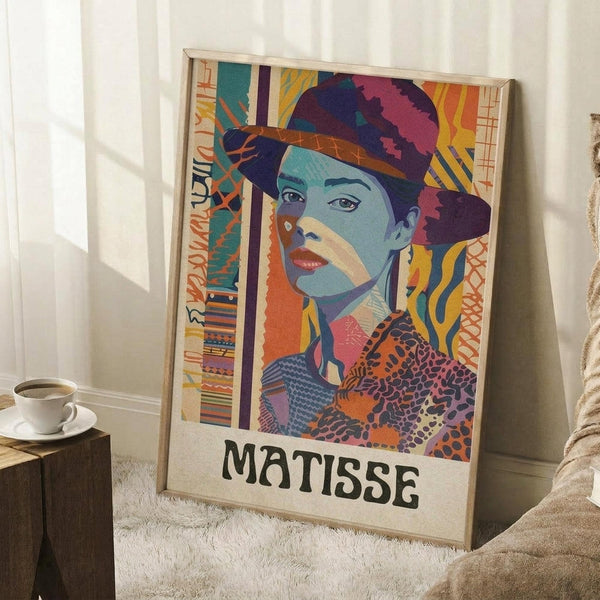 May include: Colorful artistic poster in light wood frame leaning against white wall on white fuzzy rug. Features woman with blue-tinted skin wearing dark hat, rendered in vibrant collage style with geometric patterns, stripes, and warm colors like orange, yellow, and pink. Text "MATISSE" appears at bottom. Small wooden side table with white coffee cup visible on left. Sunlight creates shadows across the scene.