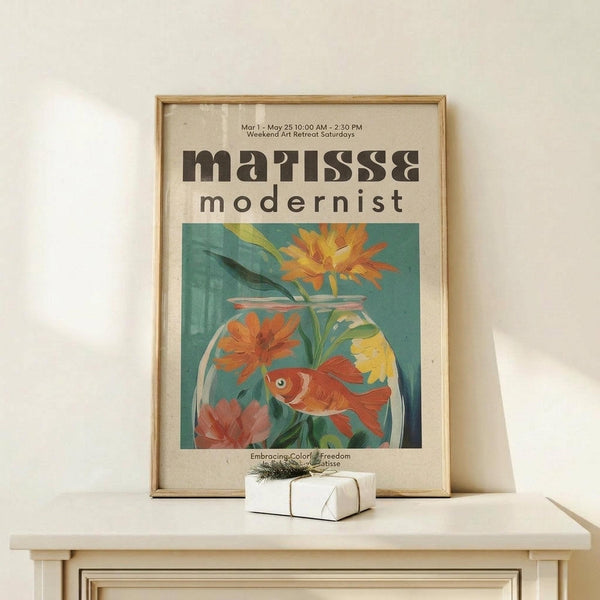 May include: Framed art print leaning against white wall on light wood shelf, featuring goldfish swimming in glass bowl with colorful flowers in teal and orange tones. Modern typography reads "matisse modernist" above the illustration. Small wrapped gift box with twine sits in front of thin natural wood frame.