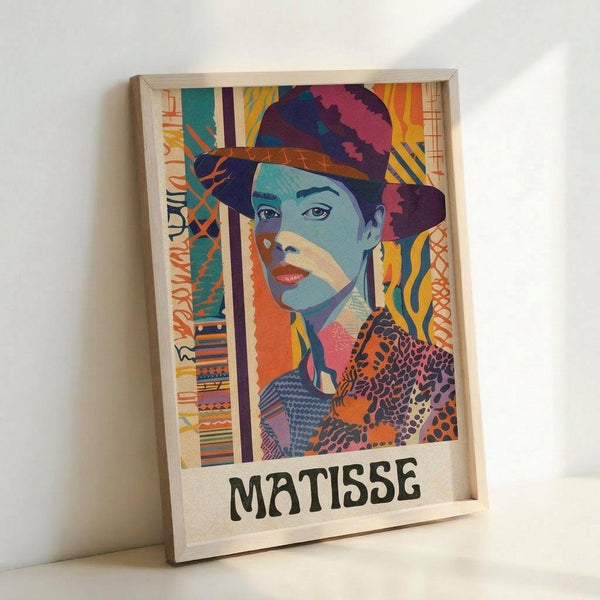 May include: Framed colorful portrait artwork leaning against white wall, featuring woman in hat rendered in vibrant blues, oranges, purples and yellows with patterned geometric elements. Light wooden frame contains vertical composition with "MATISSE" text at bottom. Bright, modern artistic style with collage-like textures and bold color blocking creates contemporary interpretation of classic portraiture.