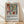 May include: Framed poster with Matisse-inspired still life artwork featuring terracotta vases with green foliage and colorful flowers in geometric panels. The print shows warm earth tones of rust, coral, and sage green with bold simplified shapes. Natural wood frame sits on light wooden floor against white textured wall with soft shadows. Black text below reads "Celebrating Colors of Life" with descriptive paragraph.