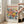 May include: Hands holding a framed poster featuring vibrant floral artwork with orange, yellow, pink and blue flowers and green leaves. The poster has "MATISSE" in large red letters at the top and "06200 NICE, FRANCE" at the bottom. Light wood frame shown in bright living room with beige sofa, white walls, and large windows casting natural sunlight on hardwood floors.