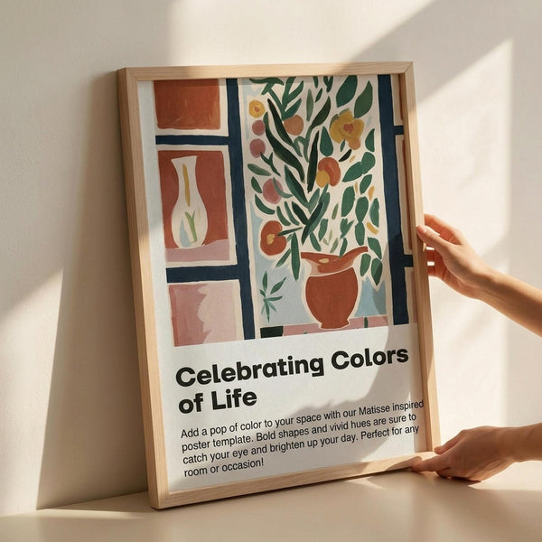 May include: Hands holding a framed poster with Matisse-inspired artwork featuring colorful vases with flowers and foliage in terracotta, green, and blue tones. The poster has "Celebrating Colors of Life" text and descriptive copy below the artwork. Natural wood frame against white wall with soft lighting and shadows.