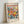 May include: Framed poster print featuring colorful floral artwork with pink, yellow, orange and coral flowers surrounded by blue-green foliage. The print displays "MATISSE" in bold red letters at the top, with "Musées Matisse" and "Tribute to a Master" text above. Bottom shows "06200 NICE, FRANCE" and exhibition details. Light wood frame sits against white wall with soft shadows.
