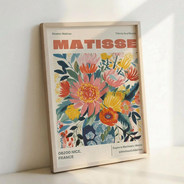 May include: Framed poster print featuring colorful floral artwork with pink, yellow, orange and coral flowers surrounded by blue-green foliage. The print displays "MATISSE" in bold red letters at the top, with "Musées Matisse" and "Tribute to a Master" text above. Bottom shows "06200 NICE, FRANCE" and exhibition details. Light wood frame sits against white wall with soft shadows.