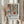 May include: Person holding framed botanical poster with abstract floral design featuring terracotta vases, green foliage, and geometric shapes in Matisse-inspired style. Natural wood frame against white curtained background with dried pampas grass stems. Warm earth tones including rust orange, sage green, and cream colors in modern artistic composition.