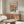 May include: A framed poster featuring vibrant cut-out style flowers in pink, yellow, orange and blue tones with "MATISSE" text at top, displayed above a mid-century modern walnut credenza with sliding doors. Scene includes a white curved lounge chair, glass oval coffee table with wooden base, and brass floor lamp in a bright, minimalist living room with cream walls and natural lighting.