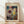 May include: Framed Paul Klee art print leaning against white wall on light wood floor. Abstract colorful artwork features geometric shapes, architectural elements, and muted tones of blue, red, yellow, purple, and green with intricate line drawings. Natural wood frame with cream matting. Soft natural lighting creates diagonal shadows across the scene.