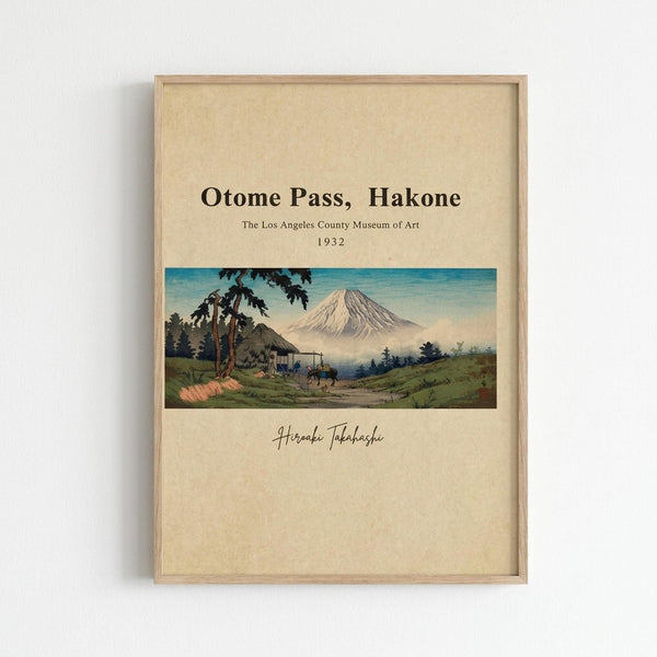 Framed vintage Japanese woodblock print reproduction showing Mount Fuji in background with rural landscape, traditional houses, and travelers on path in foreground. Artwork features muted greens, blues, and earth tones with museum-style presentation on cream background. Attribution to Hiroshi Takahashi and Los Angeles County Museum of Art 1932 included. Light wood frame mounted on white wall.
