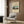 May include: Vintage Japanese travel poster print featuring Mount Fuji landscape with traditional buildings and green hills, displayed in cream-colored frame on wood paneled wall above modern beige armchair with geometric patterned pillow, brass floor lamp, and dark round side table with open book in contemporary living room setting.
