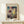 May include: Framed Paul Klee abstract art print displayed on light wood console table against cream wall. Colorful modernist artwork features geometric shapes, architectural elements, and vibrant patches of blue, red, yellow, and purple with intricate line drawings. Natural wood frame surrounds the museum poster. Small white wrapped gift with evergreen sprig sits beside the frame, creating cozy home decor scene with soft natural lighting.