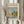 May include: Hands holding a framed Claude Monet exhibition poster featuring his 1872 painting "Regattas at Argenteuil" showing sailboats on blue water with reflections and green trees. One hand also holds dried wheat stalks. The poster has cream matting with black text and sits against white curtains in soft natural lighting.