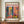 May include: Framed art print featuring vibrant Matisse-style interior scene with colorful plants, furniture, and artwork in pink, blue, yellow, and green tones. Print displays "MATISSE" text and "06200 NICE, FRANCE" at bottom. Frame sits on wooden surface beside white ceramic vase and stacked books against cream wall with decorative molding.
