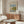 May include: Framed Claude Monet exhibition poster showing sailboats on water in impressionist style, displayed above walnut credenza in minimalist living room with cream chair, glass coffee table, and modern lighting fixtures on neutral walls.