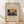 May include: Framed art print leaning against white wall on light wood floor with soft natural lighting and shadows. Features colorful abstract landscape with blue mountains, rainbow, tree, and geometric shapes in Kandinsky's style. Cream matting with wooden frame, styled in minimalist interior setting.