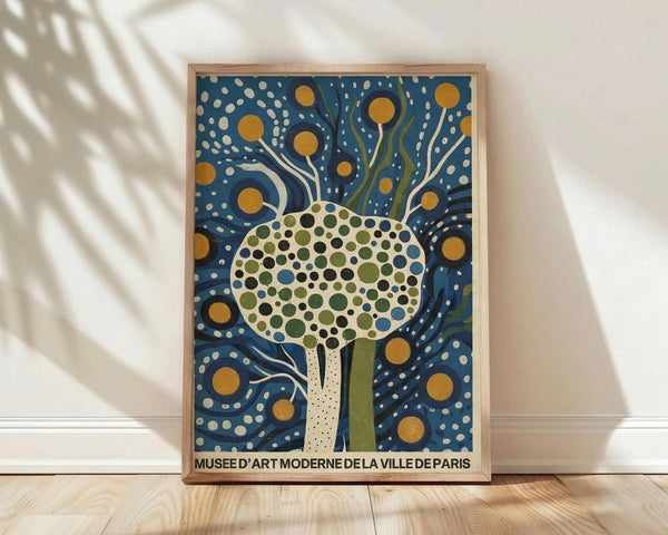May include: Framed art print leaning against white wall on light wood flooring with palm leaf shadows. Features stylized tree with dotted circular canopy in green, blue and black dots on cream background. Deep blue starry night sky surrounds tree with golden yellow orbs and flowing white lines. Natural wood frame. Museum text at bottom in black letters.