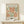 May include: Framed vintage-style art poster featuring abstract orange and sage green organic shapes in Matisse's cut-out style, displayed on light wood surface with small wrapped gift box, against cream wall in modern interior setting