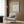 May include: Sage green and white Matisse-inspired botanical poster displayed in modern living room with beige upholstered armchair, geometric patterned pillow, brass floor lamp, and wood wall paneling. Abstract flower cutout design with white petals on muted green background in light wood frame.